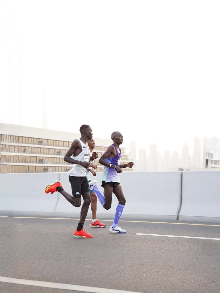Cheptegei, Kipkorir, and Simbu running closely together mid-race at the 2026 Burj2Burj Half Marathon in Dubai.