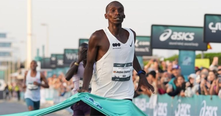 Joshua Cheptegei crossing the finish line, raising his arms in triumph at the 2026 Burj2Burj Half Marathon.